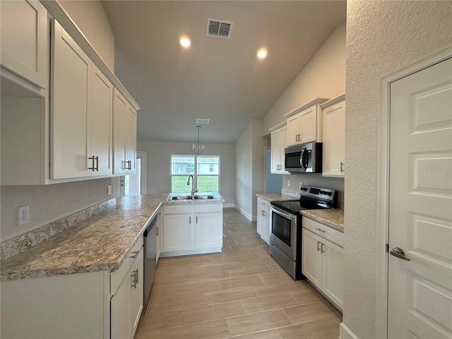 kitchen with appliances with stainless steel finishes, decorative light fixtures, white cabinetry, sink, and kitchen peninsula