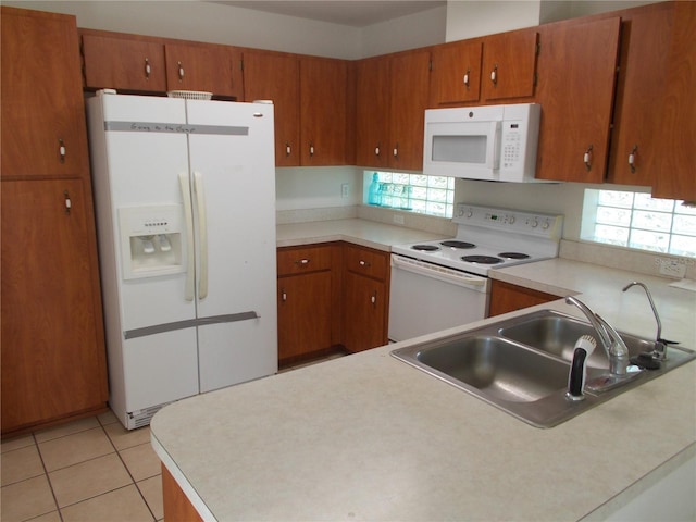 kitchen with brown cabinetry, white appliances, light countertops, and a sink