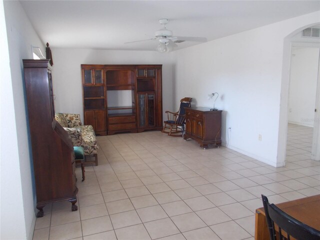 living area featuring a ceiling fan, visible vents, baseboards, light tile patterned flooring, and arched walkways