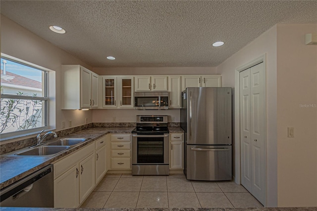 kitchen featuring sink, light tile patterned floors, appliances with stainless steel finishes, white cabinetry, and a textured ceiling