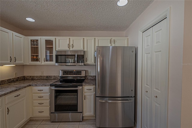 kitchen with stainless steel appliances, light tile patterned flooring, white cabinets, and a textured ceiling