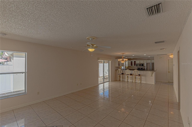 unfurnished living room featuring light tile patterned floors, ceiling fan with notable chandelier, a wealth of natural light, and a textured ceiling