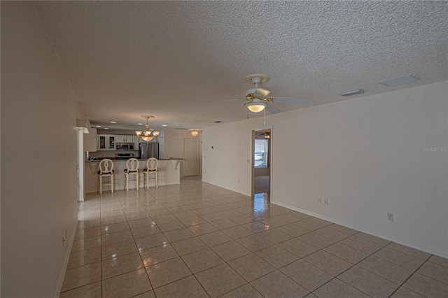 tiled empty room featuring ceiling fan with notable chandelier and a textured ceiling