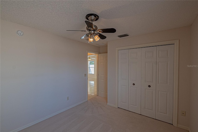 unfurnished bedroom with ceiling fan, light carpet, a textured ceiling, and a closet