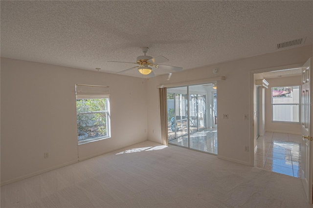 empty room featuring ceiling fan, a textured ceiling, light carpet, and a wealth of natural light