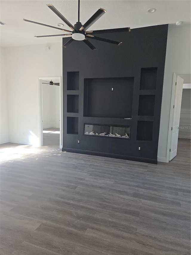 unfurnished living room featuring dark hardwood / wood-style flooring, built in shelves, and ceiling fan