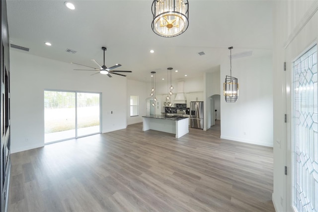 unfurnished living room featuring ceiling fan with notable chandelier, a towering ceiling, and light wood-type flooring