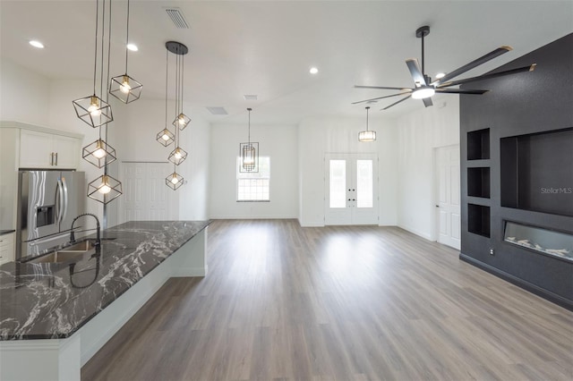 kitchen featuring sink, hanging light fixtures, stainless steel fridge, dark stone counters, and white cabinets