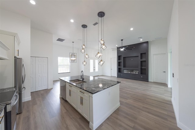 kitchen with decorative light fixtures, white cabinetry, sink, dark stone counters, and a kitchen island with sink