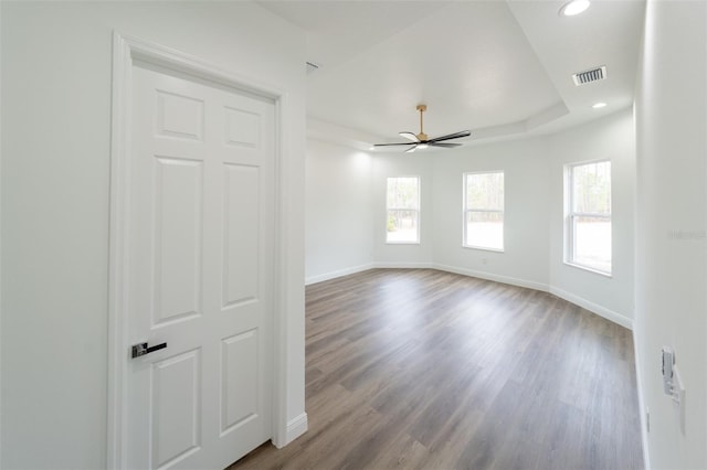 unfurnished room with ceiling fan, a healthy amount of sunlight, light wood-type flooring, and a tray ceiling