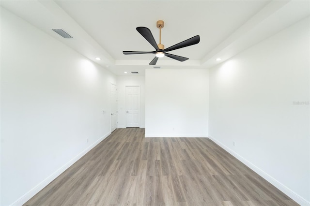 spare room featuring a tray ceiling, ceiling fan, and light wood-type flooring