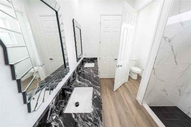 bathroom featuring hardwood / wood-style flooring, vanity, a tile shower, and toilet