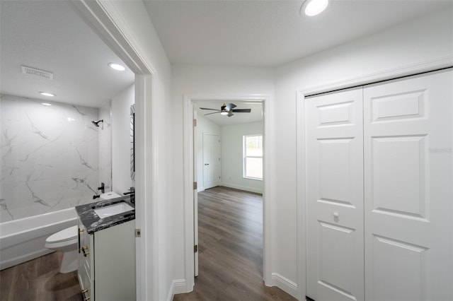 full bathroom featuring hardwood / wood-style flooring, vanity, tiled shower / bath combo, and toilet