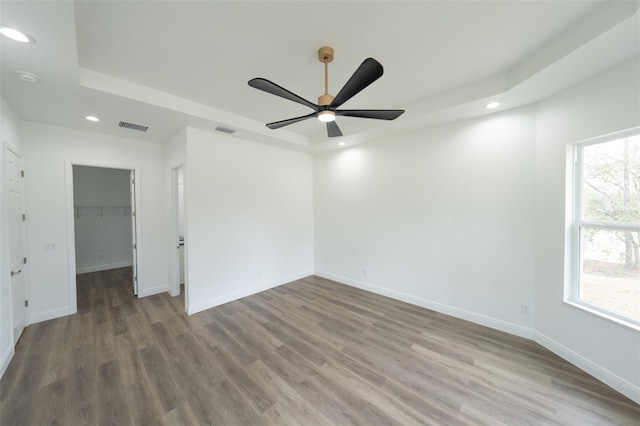 empty room with hardwood / wood-style flooring, ceiling fan, and a raised ceiling