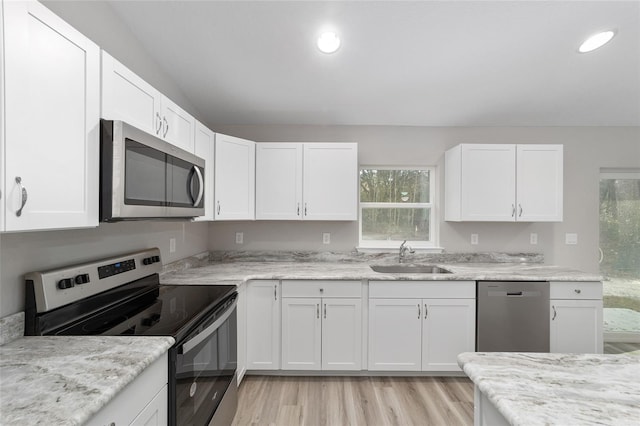 kitchen with appliances with stainless steel finishes, sink, white cabinets, light stone counters, and light hardwood / wood-style flooring