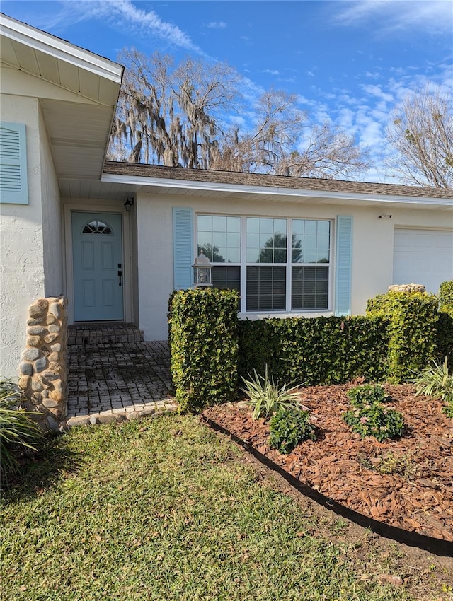 view of exterior entry with a garage and stucco siding