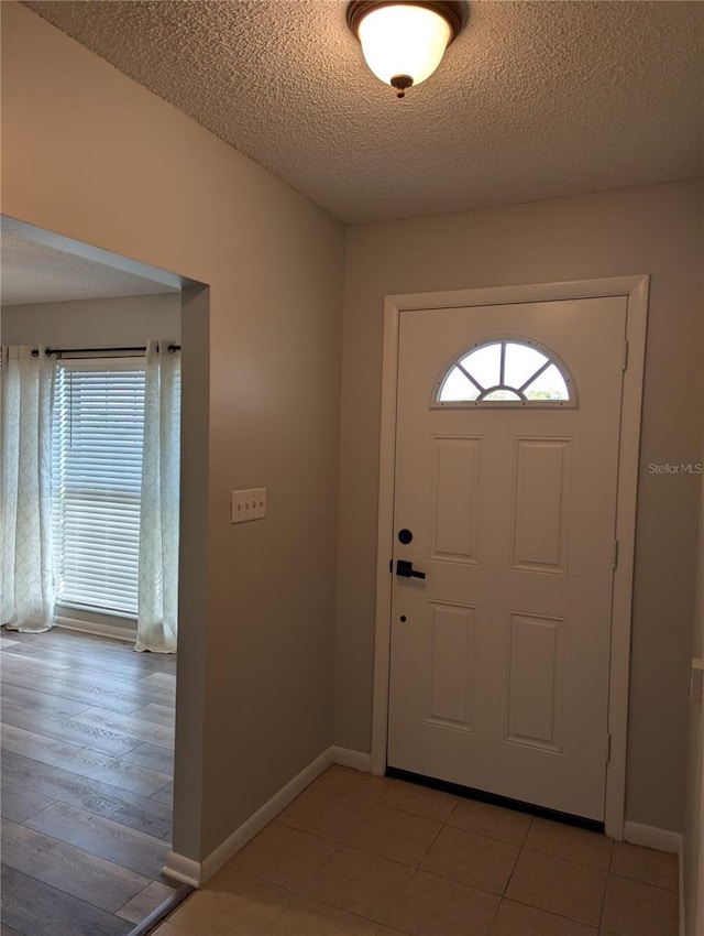 foyer featuring light tile patterned flooring, a textured ceiling, and baseboards