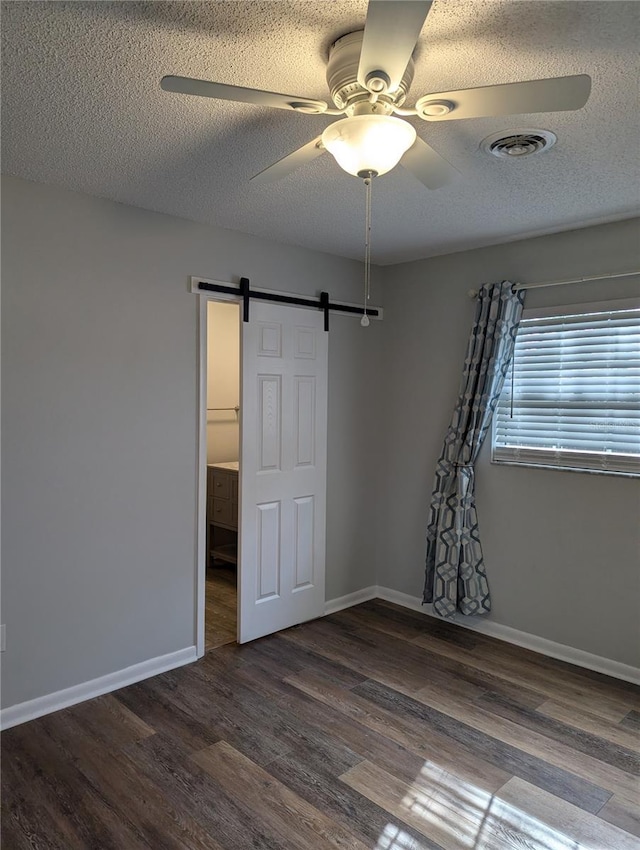 spare room with a textured ceiling, a barn door, wood finished floors, visible vents, and baseboards