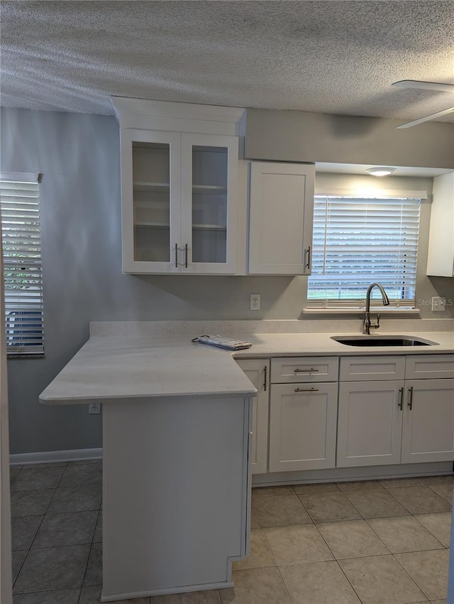 kitchen featuring light countertops, glass insert cabinets, white cabinets, a sink, and a textured ceiling