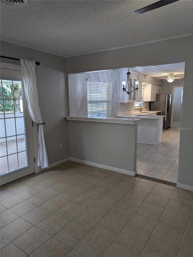 interior space featuring light tile patterned floors, white cabinets, freestanding refrigerator, light countertops, and ceiling fan with notable chandelier