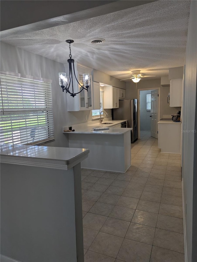 kitchen featuring light countertops, freestanding refrigerator, white cabinets, a chandelier, and a peninsula