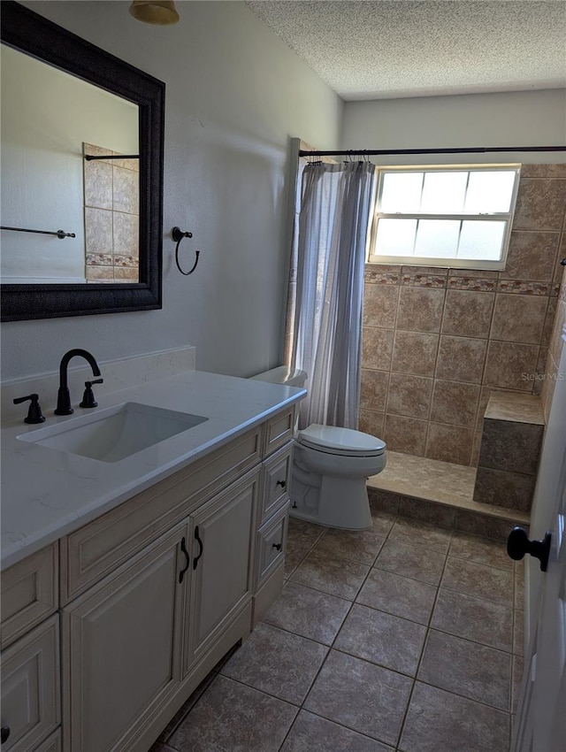 full bath featuring a tile shower, a textured ceiling, toilet, and vanity