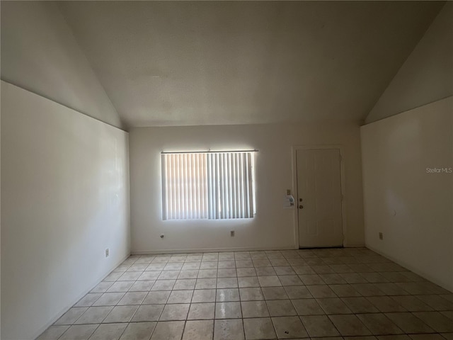 tiled empty room featuring lofted ceiling