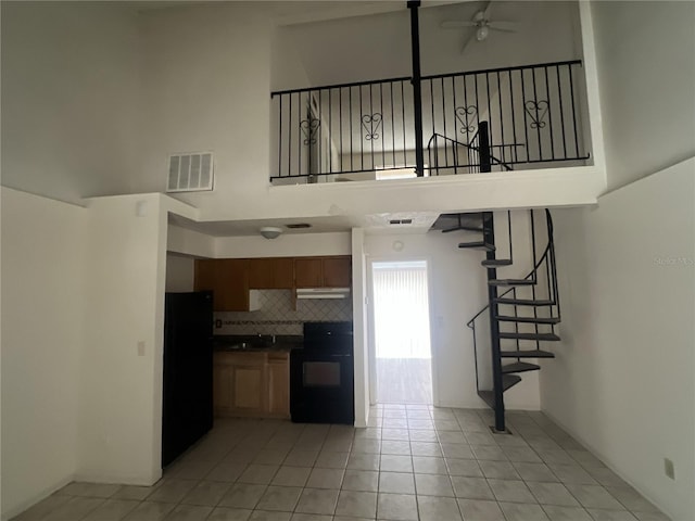 kitchen with black fridge, electric range, ceiling fan, a high ceiling, and backsplash