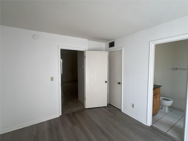 unfurnished bedroom with ensuite bathroom, dark hardwood / wood-style flooring, and a textured ceiling