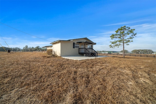 exterior space featuring a yard, a rural view, fence, and stucco siding