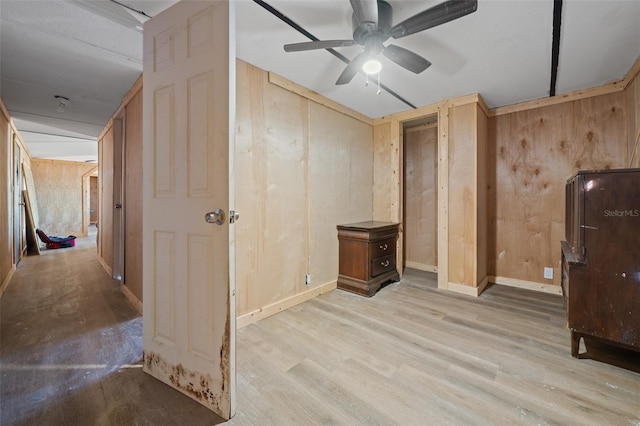 interior space with wooden walls, ceiling fan, light wood-style flooring, and baseboards