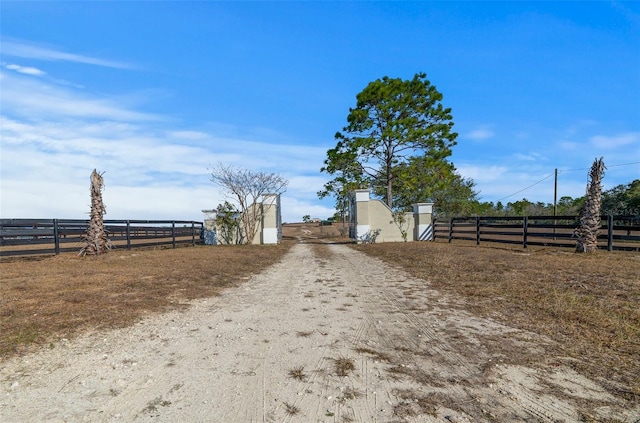 view of road featuring dirt driveway, a gated entry, and a rural view