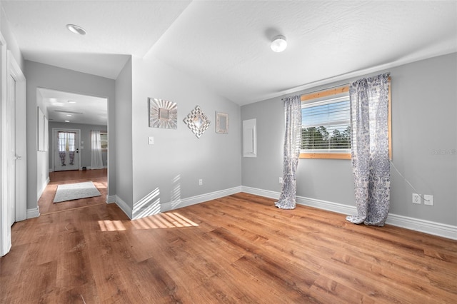 unfurnished room featuring lofted ceiling, baseboards, and wood finished floors