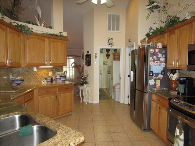 kitchen with light tile patterned flooring, appliances with stainless steel finishes, light stone countertops, and tasteful backsplash