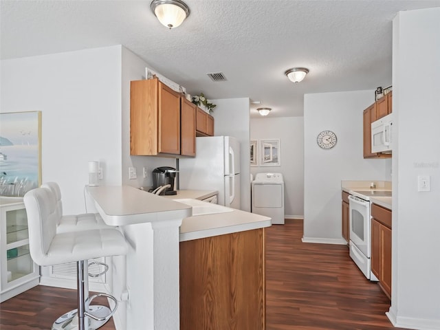 kitchen with white appliances, a kitchen breakfast bar, dark hardwood / wood-style flooring, washer / dryer, and kitchen peninsula