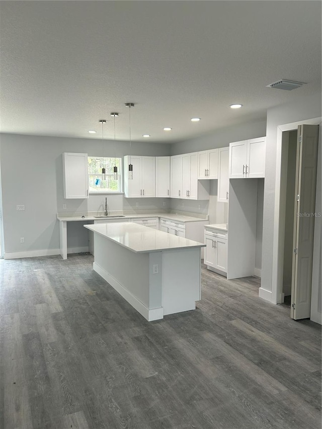 kitchen with dark wood-type flooring, visible vents, a center island, and a sink