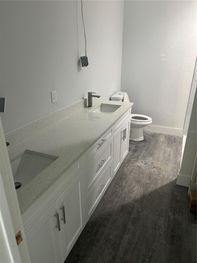 bathroom featuring toilet, a sink, wood finished floors, baseboards, and double vanity