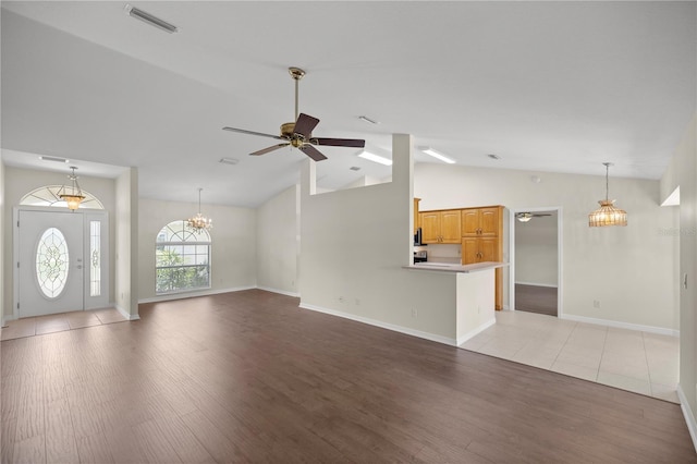 unfurnished living room with ceiling fan with notable chandelier, vaulted ceiling, and light wood-type flooring