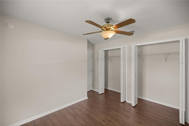 unfurnished bedroom featuring multiple closets, dark hardwood / wood-style floors, and ceiling fan