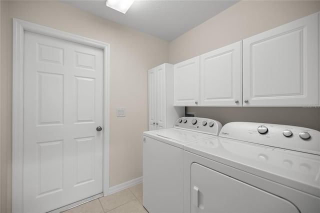 clothes washing area with washing machine and dryer, cabinets, and light tile patterned flooring