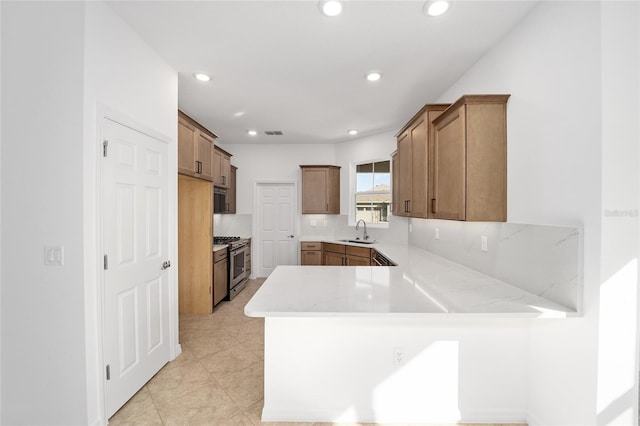 kitchen with sink, light stone counters, gas stove, decorative backsplash, and kitchen peninsula