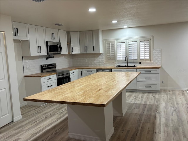 kitchen featuring wood counters, appliances with stainless steel finishes, a center island, and sink