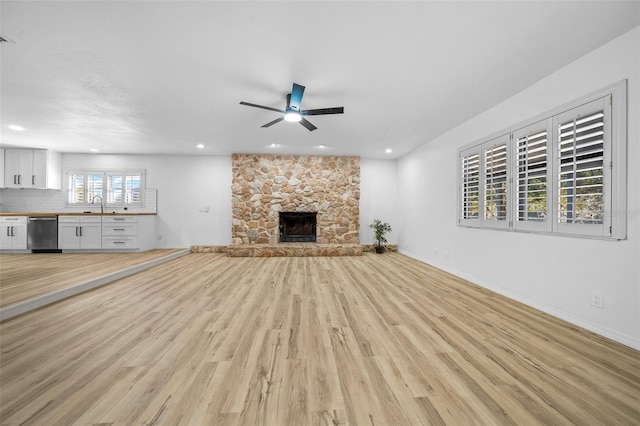 unfurnished living room featuring ceiling fan, a stone fireplace, sink, and light wood-type flooring