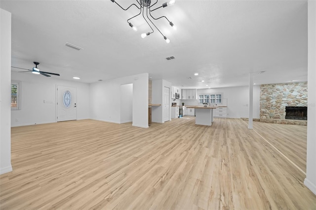 unfurnished living room featuring a stone fireplace, light hardwood / wood-style floors, ceiling fan, and a textured ceiling