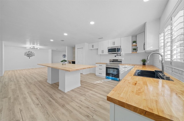 kitchen with stainless steel appliances, sink, white cabinets, and butcher block countertops