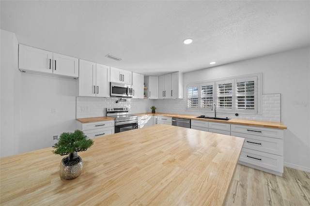 kitchen with sink, appliances with stainless steel finishes, butcher block counters, backsplash, and white cabinets