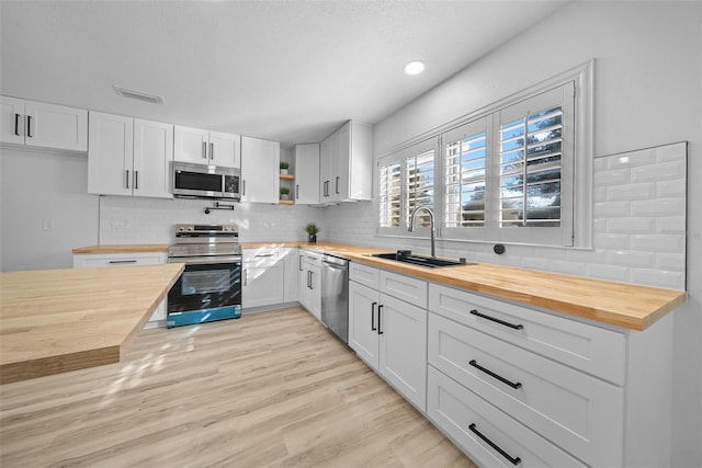 kitchen with butcher block countertops, sink, white cabinets, and appliances with stainless steel finishes