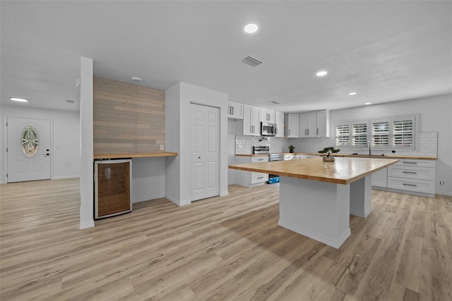 kitchen with butcher block countertops, appliances with stainless steel finishes, white cabinetry, decorative backsplash, and beverage cooler