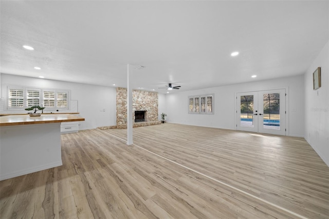 unfurnished living room with french doors, ceiling fan, a fireplace, and light wood-type flooring