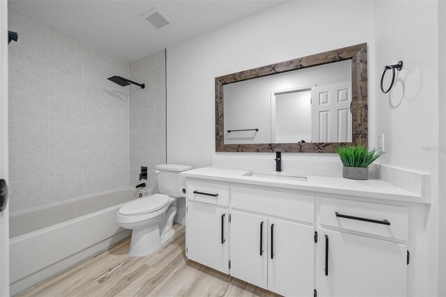 full bathroom featuring vanity, hardwood / wood-style floors, tiled shower / bath combo, and toilet